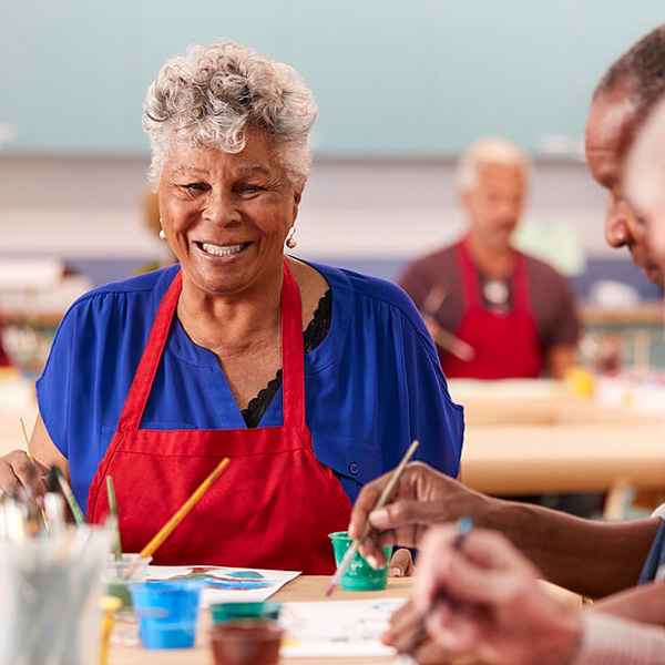 Smiling senior woman in a red apron painting in an art class with fellow seniors.