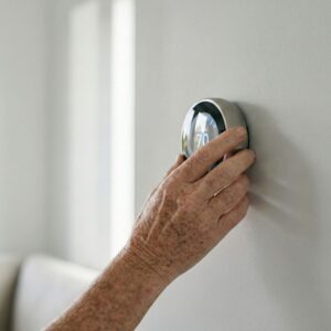 A hand adjusting a smart thermostat mounted on a wall.