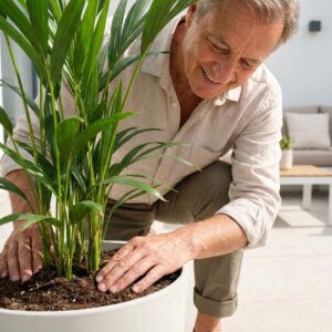 A smiling person tending to a potted plant on a bright patio.